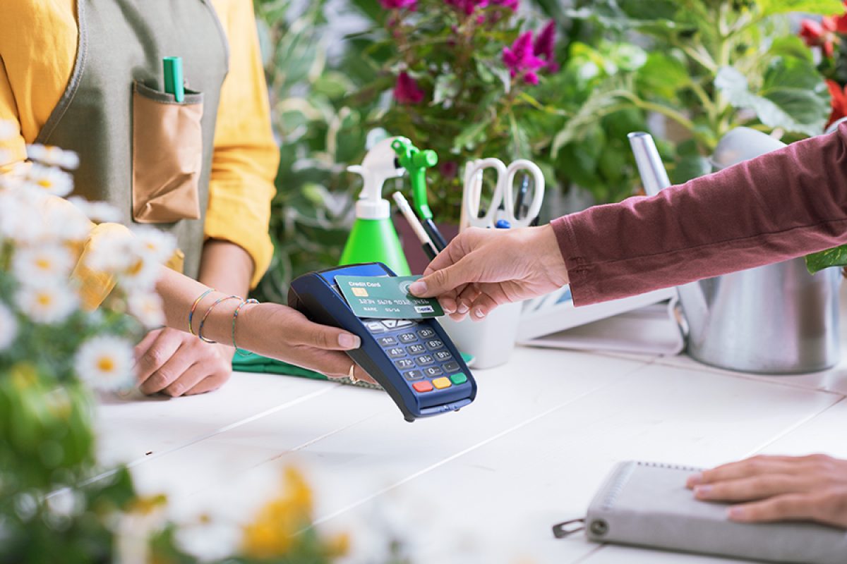 Customer at the florist shop, she is paying with her credit card, the shop owner is holding the POS terminal, hands close up